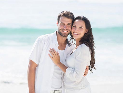 couple at the beach | Pollock Advanced Dental Group woman smiling and showing her white teeth